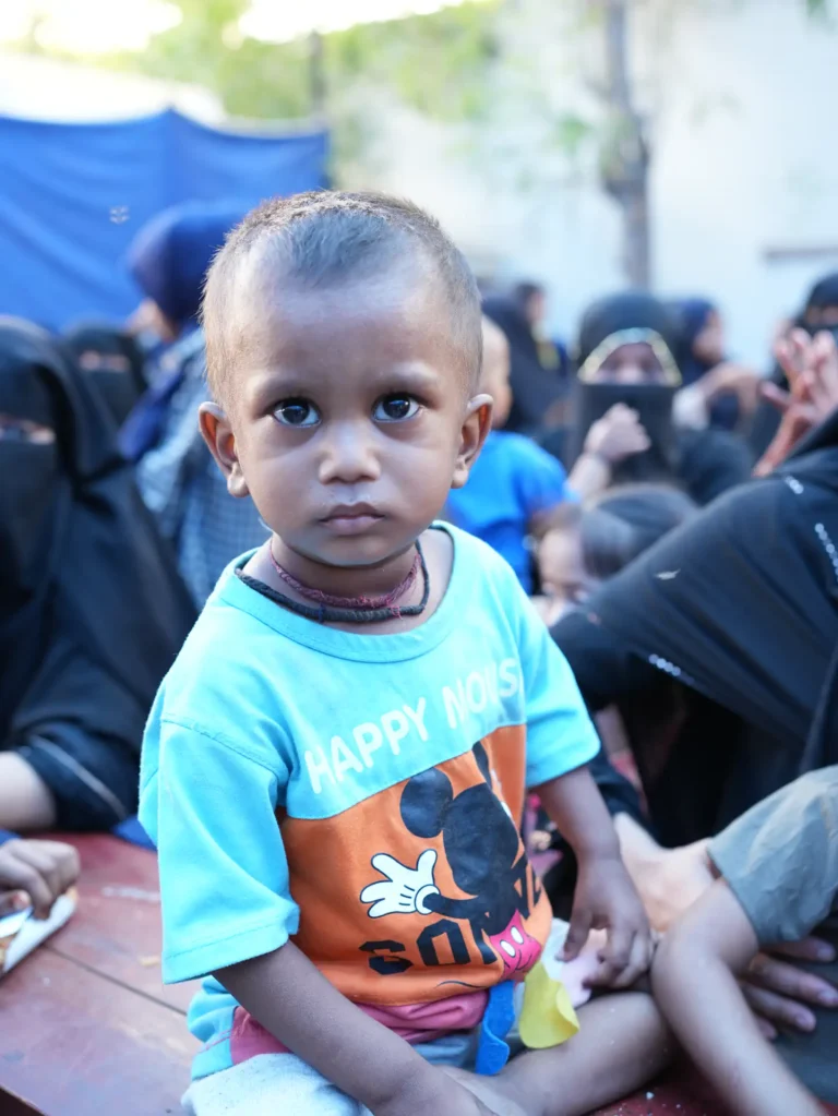 A young child sitting among mothers waiting at a ZMT health camp