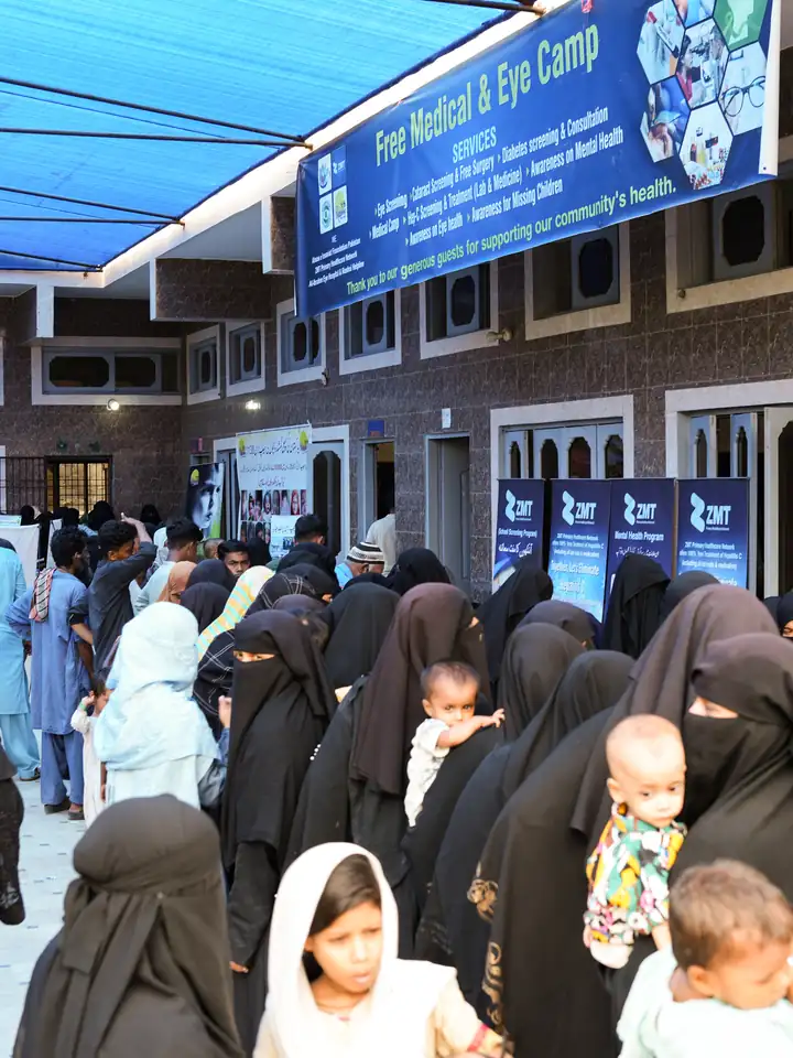 Families queueing under a banner at a ZMT medical and eye camp
