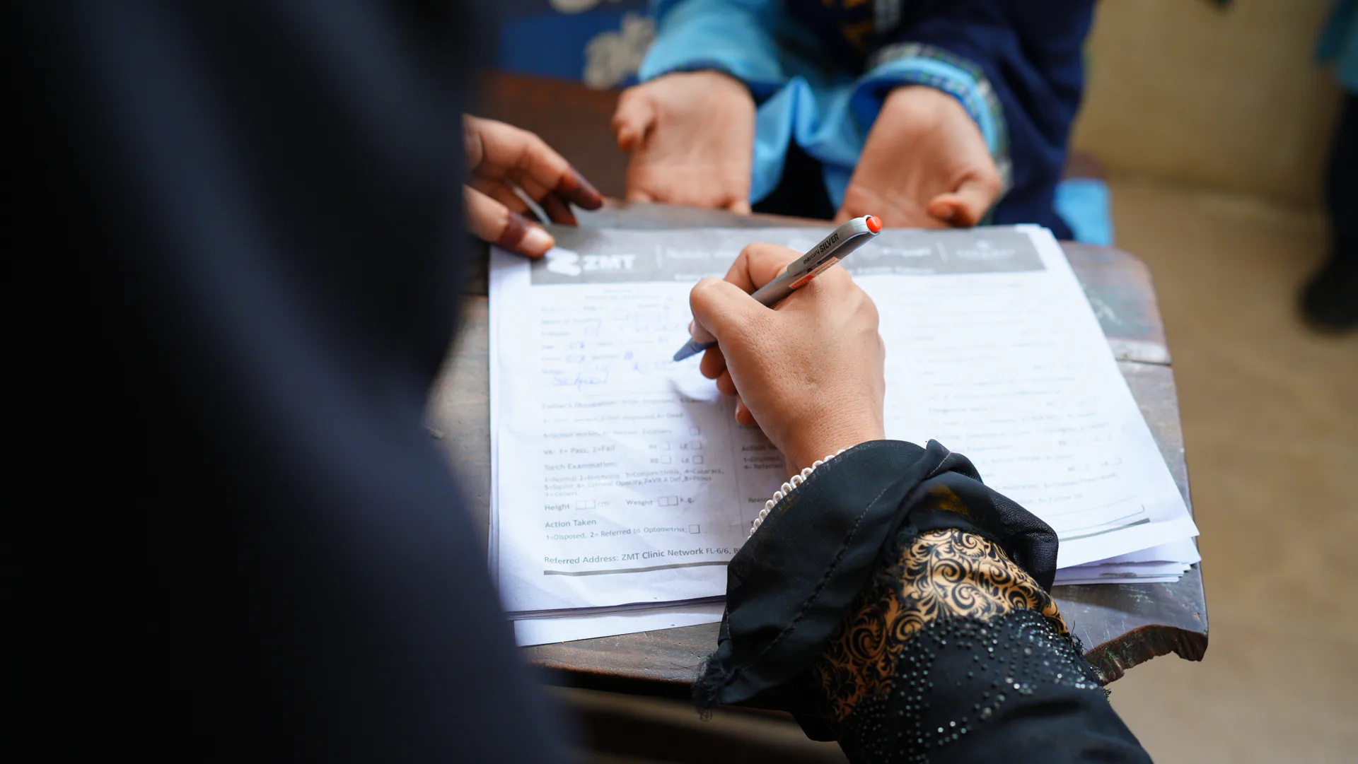 A ZMT staff member filling in a patient registration form at a clinic desk