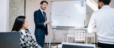 Presenter pointing to a growth chart on a whiteboard during a CSR reporting meeting