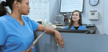 Two nurses talking at a hospital reception desk, the staff ongoing charity keeps in work