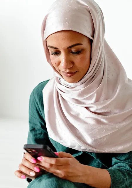 Woman in a hijab using her smartphone, as you would to pay zakat online